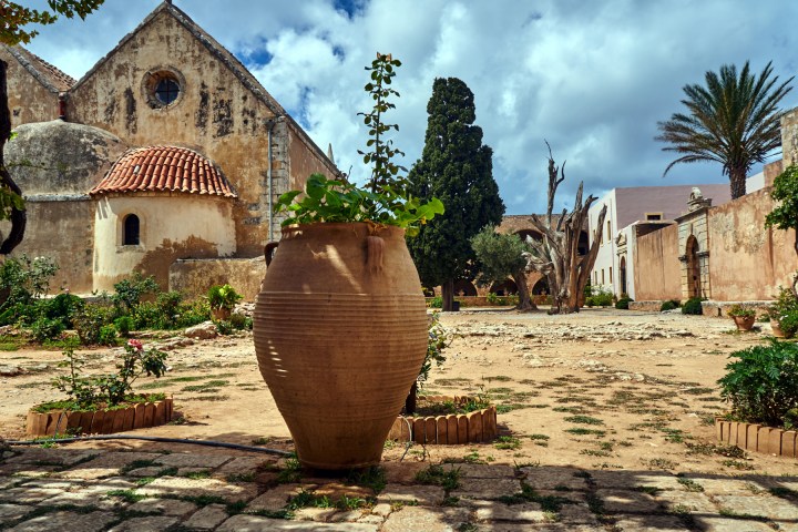 a close up of a stone building that has trees around it with Carmel Mission Basilica in the background